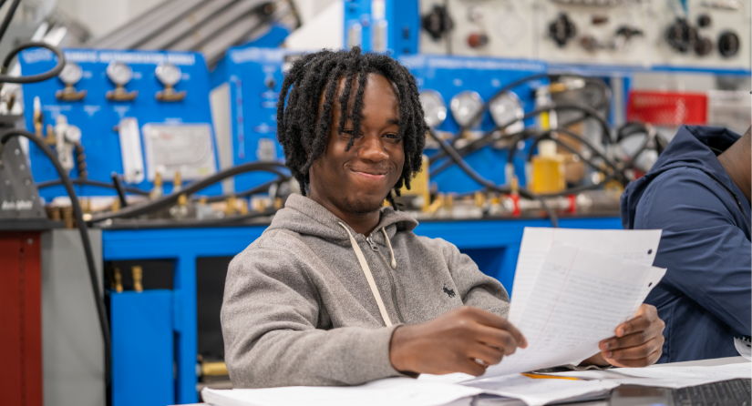 A student seated at a table reviewing a piece of paper and smiling