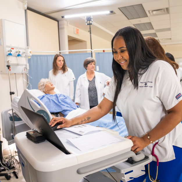 A person looking at a computer screen in a hospital training room with others gathered in the background.