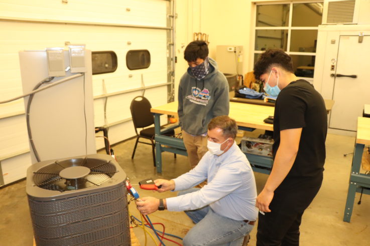 A man demonstrating checking an air conditioning unit with students watching him.