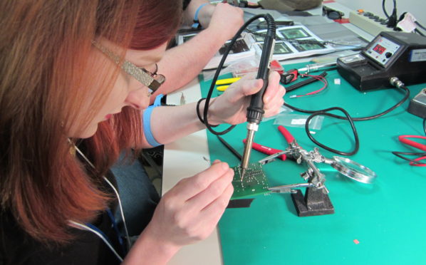 A woman using a soldering iron on a circuit board