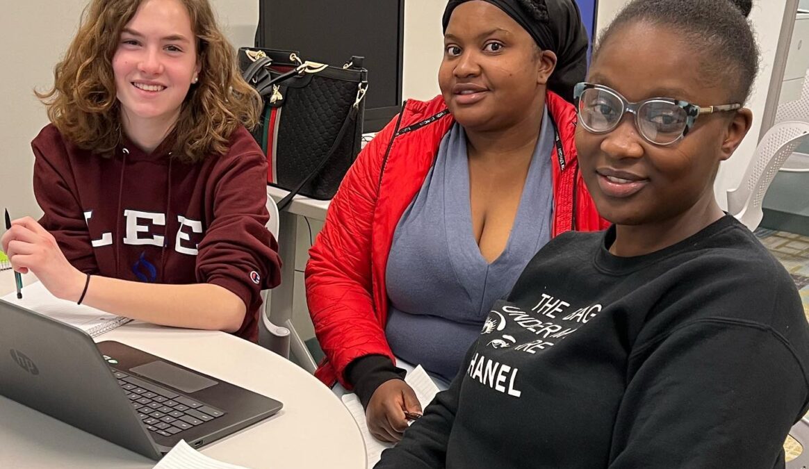 Three students seated at a desk with a laptop in front of them.