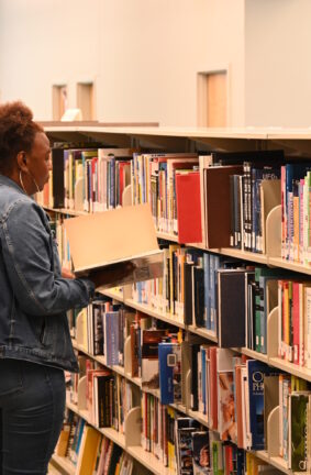A woman looking at a book in front of a row of bookshelves