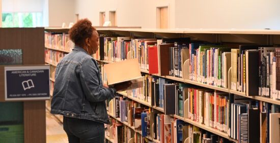 A woman looking at a book in front of a row of bookshelves