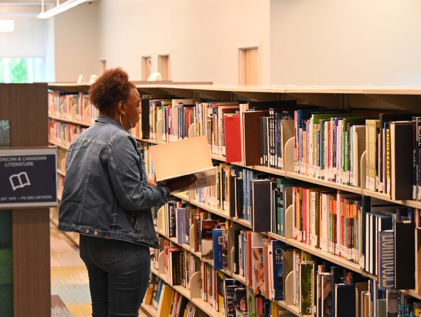 A woman looking at a book in front of a row of bookshelves