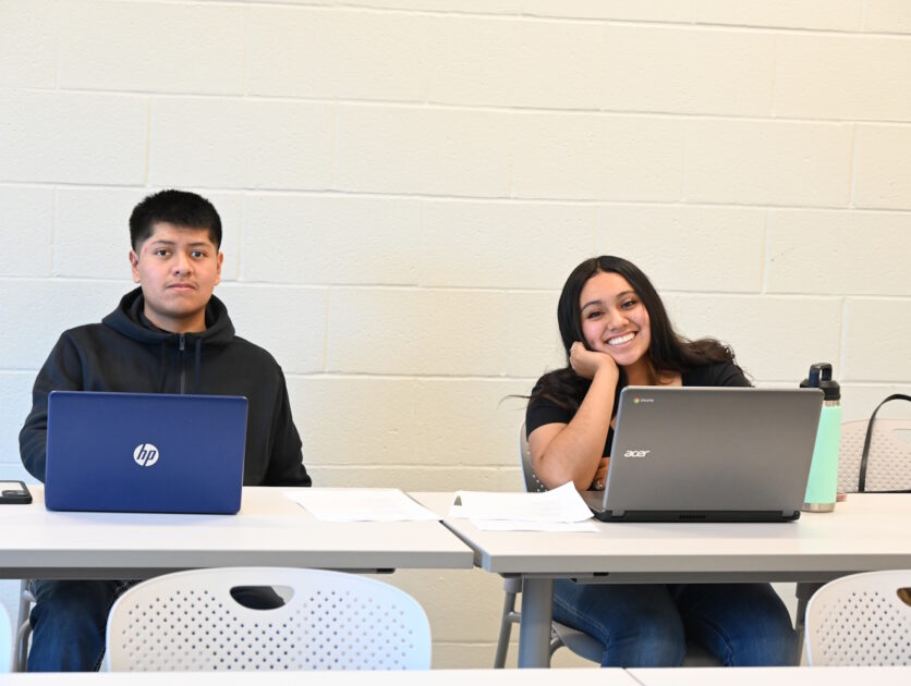 Two people seated at tables and using laptops