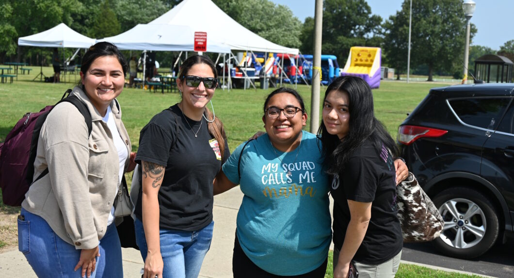 A group of four women standing outside near a parking lot with a large tent behind them.