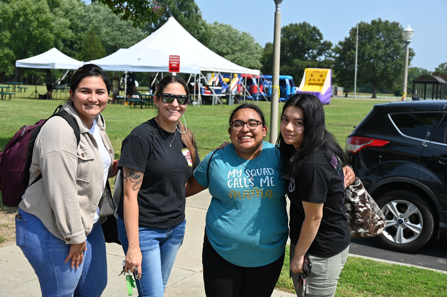 A group of four women standing outside near a parking lot with a large tent behind them.