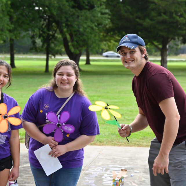 Three people standing outside holding artificial flowers