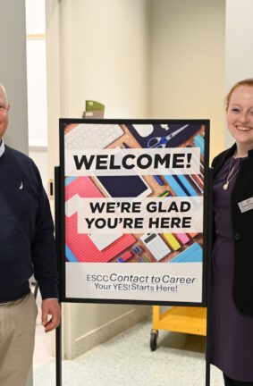 Two people standing beside a Welcome to ESCC sign