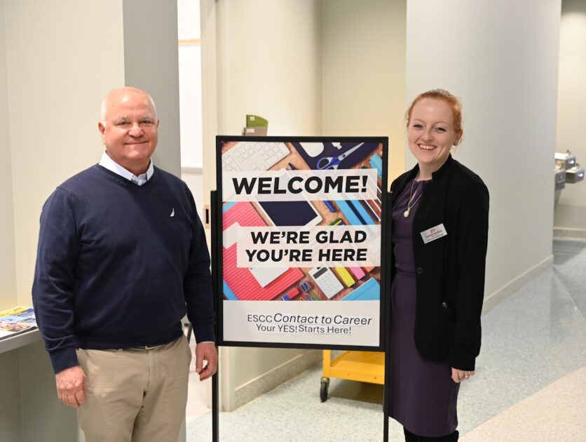 Two people standing beside a Welcome to ESCC sign