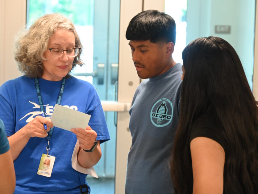 A woman holding an index card and showing it to two people