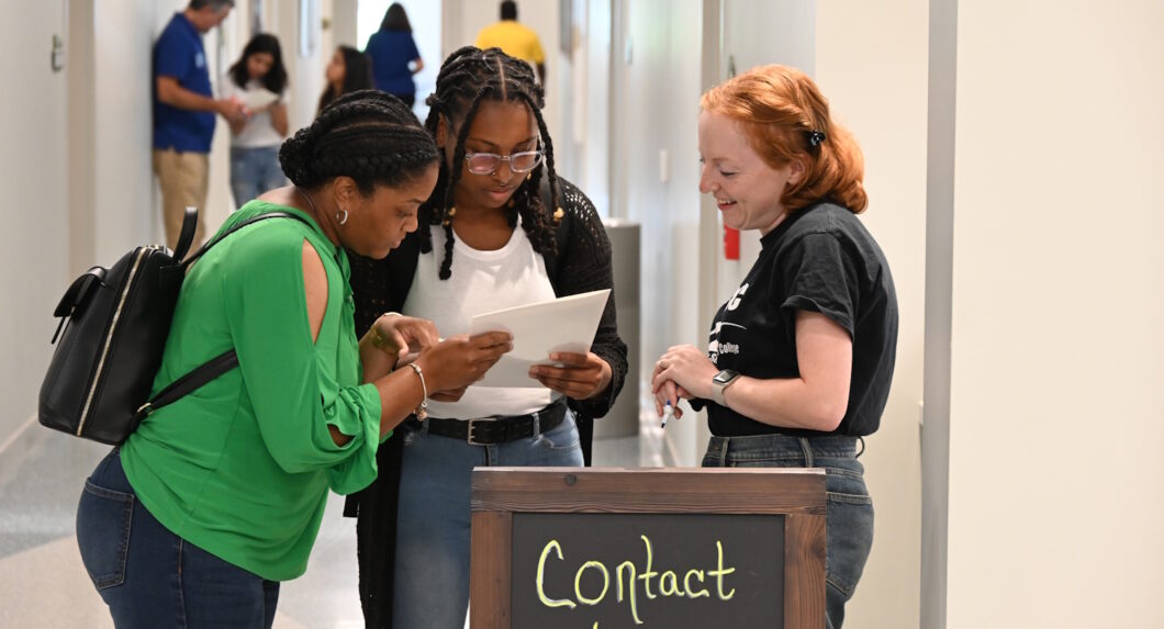 Three women looking at some papers while standing in a hallway