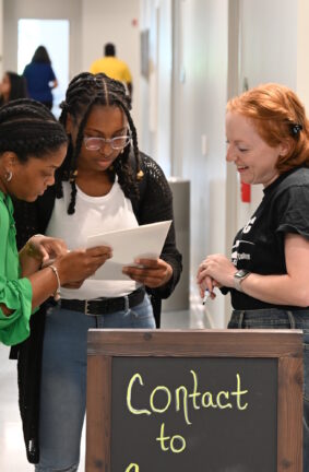 Three women looking at some papers while standing in a hallway