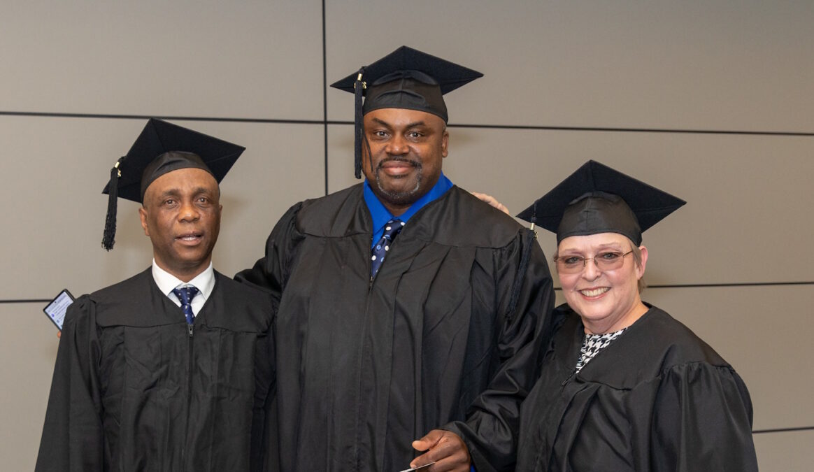 Three people wearing graduation caps and gowns standing in front of a wall.