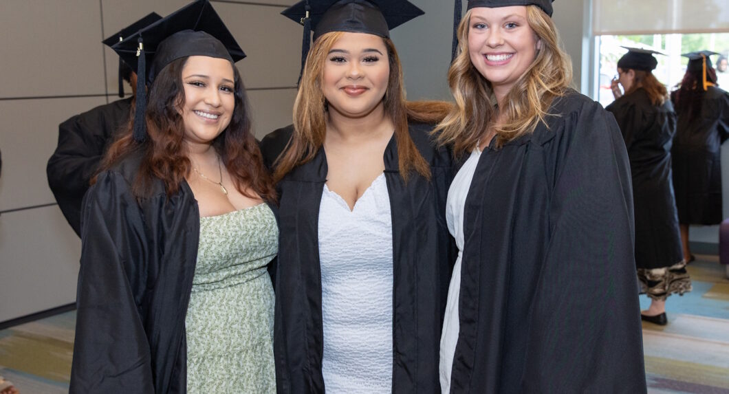 Three women wearing graduation caps and gowns and standing in a hallway.