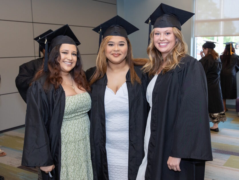 Three women wearing graduation caps and gowns and standing in a hallway.