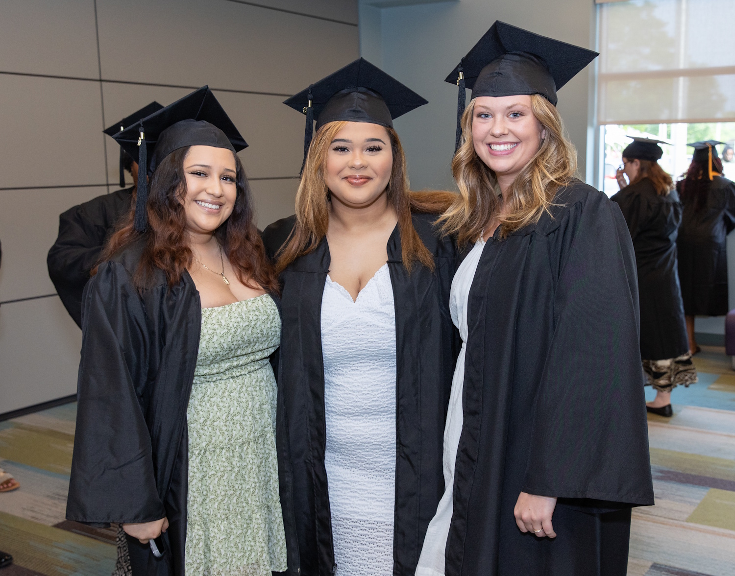 Three women wearing graduation caps and gowns and standing in a hallway.