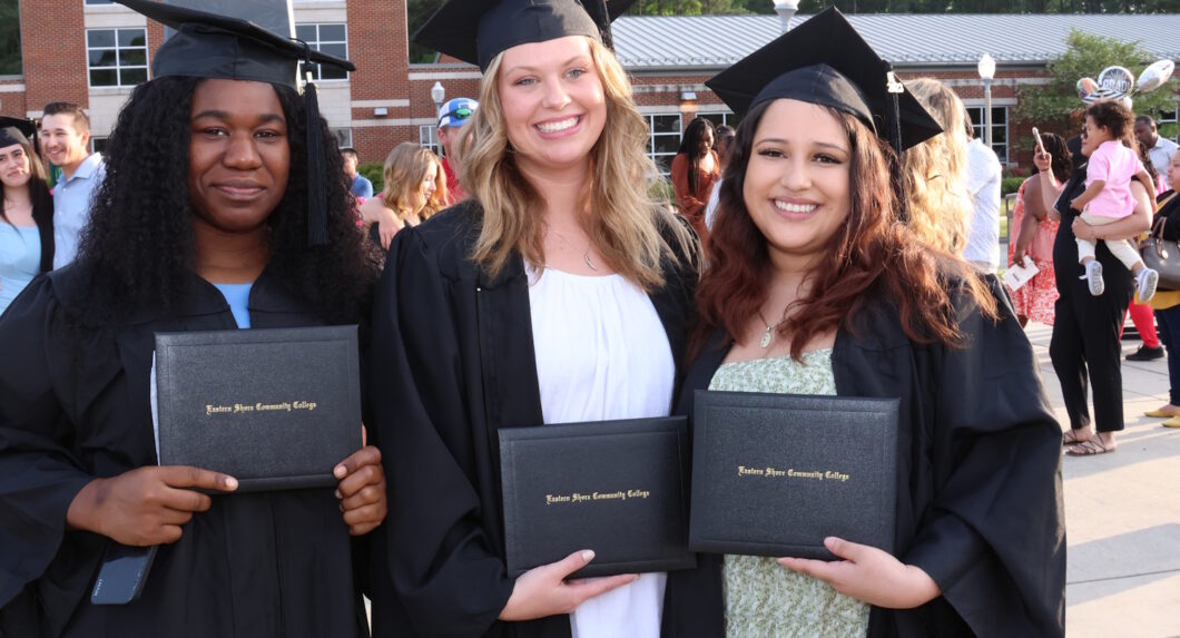 Three people wearing graduation caps and gowns and holding their diplomas