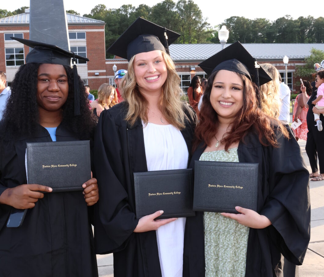 Three people wearing graduation caps and gowns and holding their diplomas