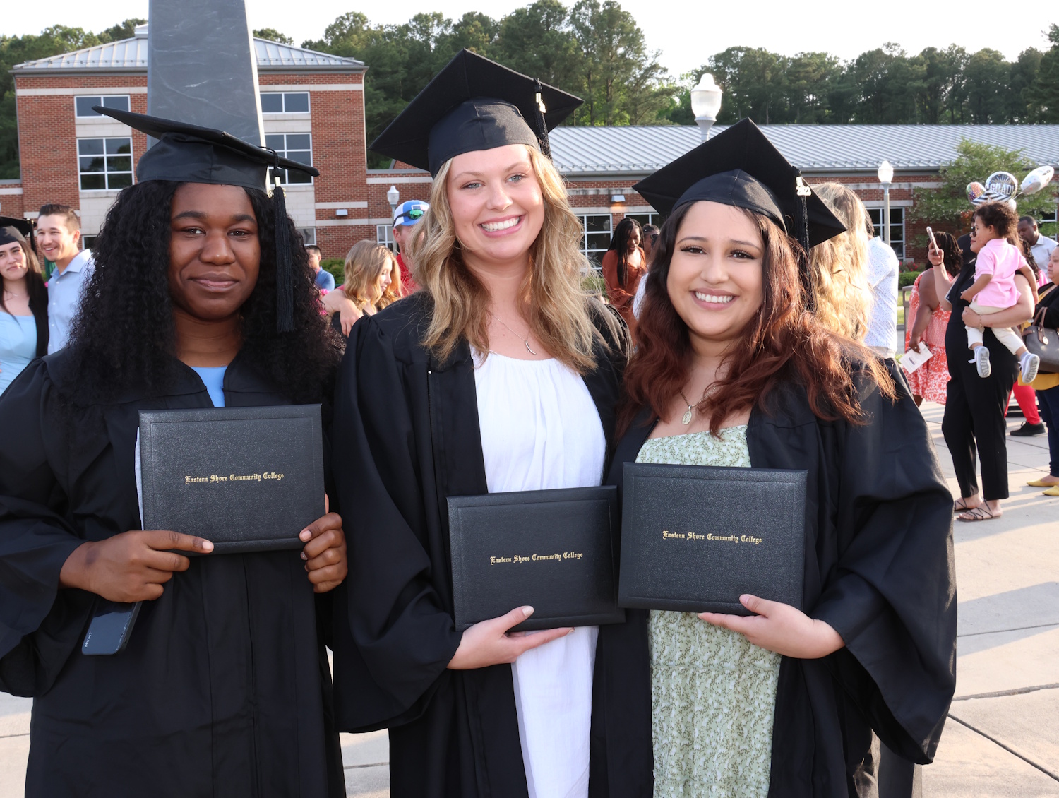 Three people wearing graduation caps and gowns and holding their diplomas
