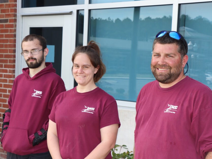 Three people standing outside of a campus building.