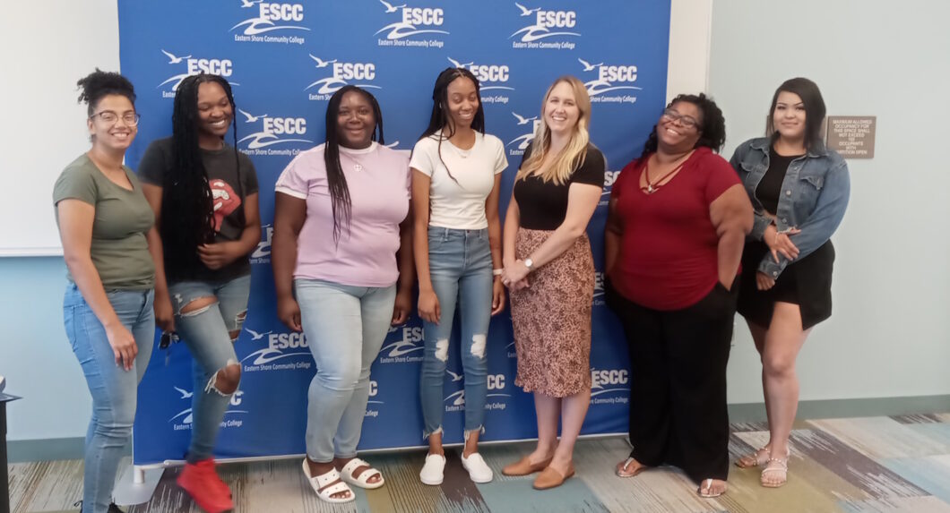 A group of women standing in front of a banner with the Eastern Shore Community College logo on it.