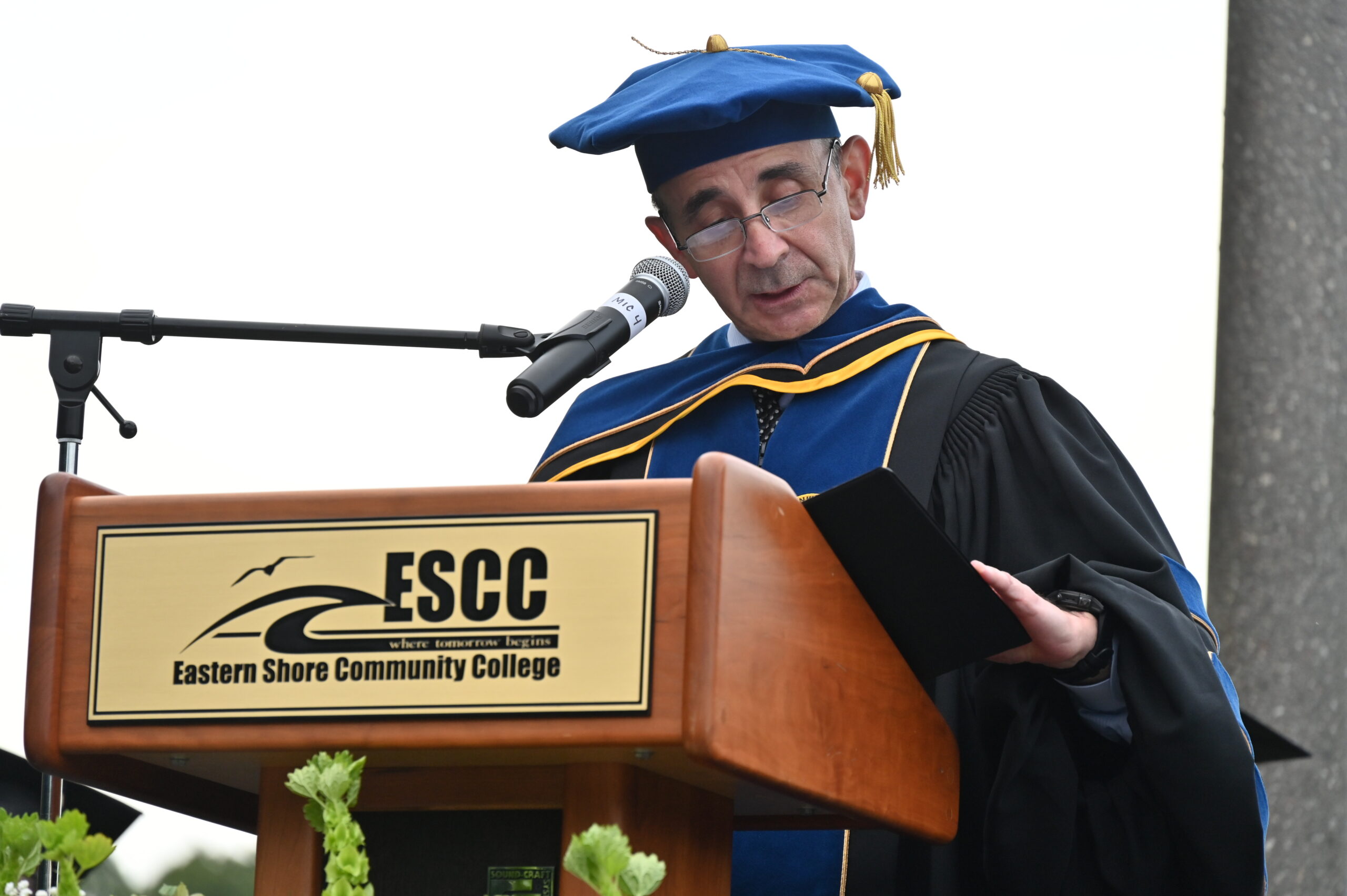 A man wearing a cap and gown standing at a podium with a microphone